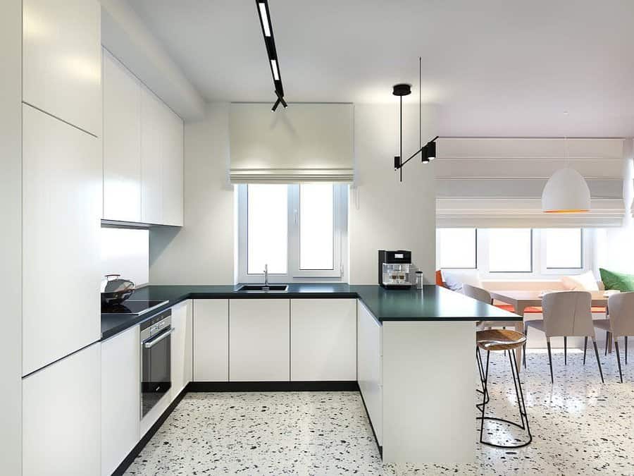 Modern kitchen with white cabinets, black countertops, and terrazzo flooring; dining area with chairs and pendant lighting nearby