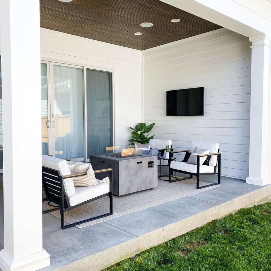 Modern patio with white cushioned chairs, a concrete coffee table, TV on shiplap wall, sliding glass door, and a wooden ceiling