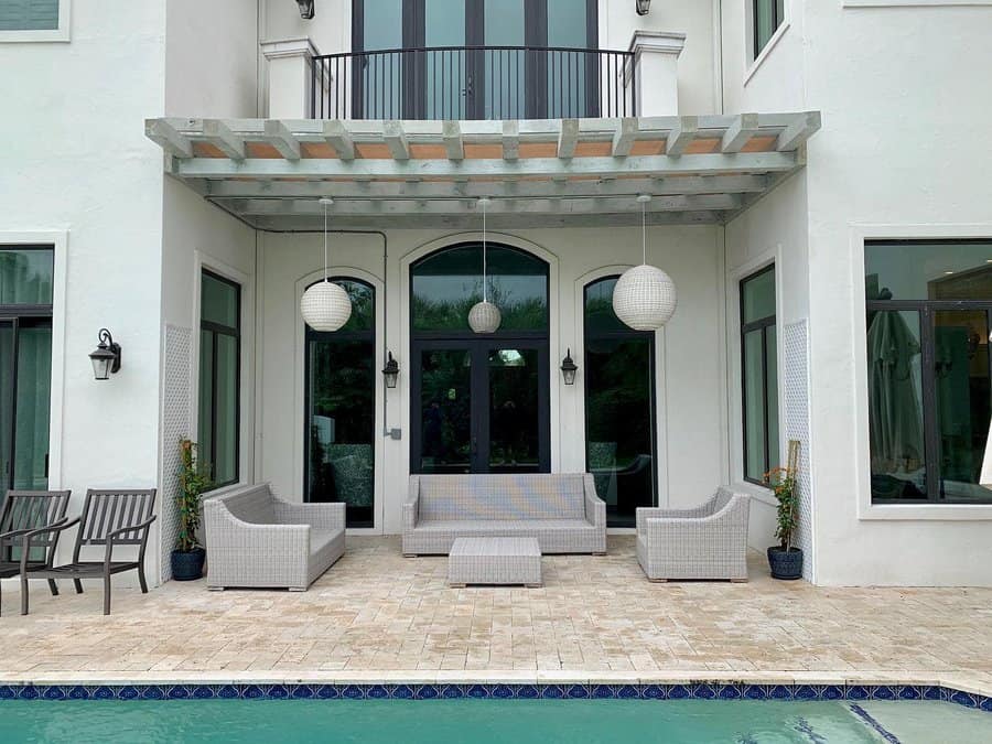 Modern patio with gray seating, round hanging lights, and a pool; large glass doors and windows on a white building