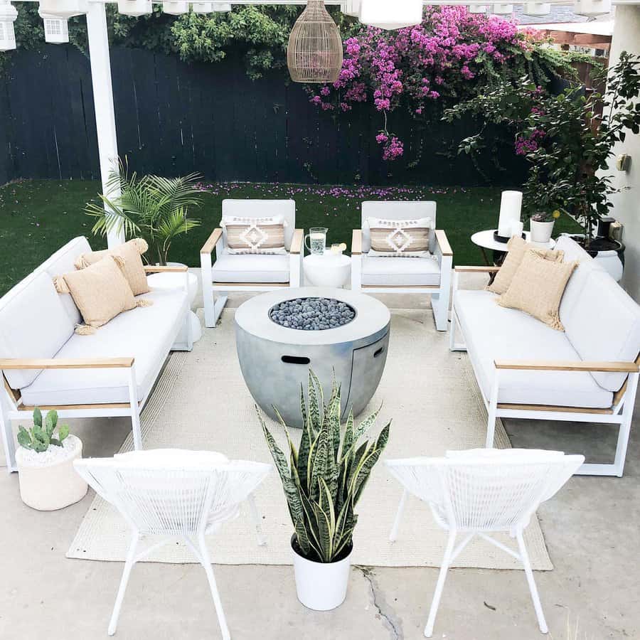 Outdoor patio with white sofas, a fire pit, plants, and purple flowers