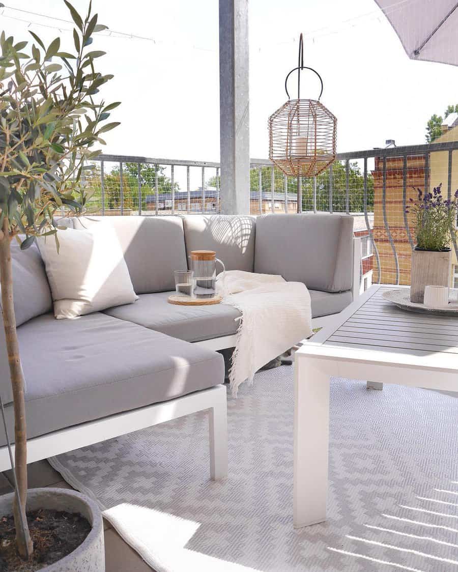 Minimalist small balcony with a gray L-shaped outdoor sofa, white coffee table, and a cozy neutral-toned rug. A hanging rattan lantern and potted plants enhance the modern, serene atmosphere.