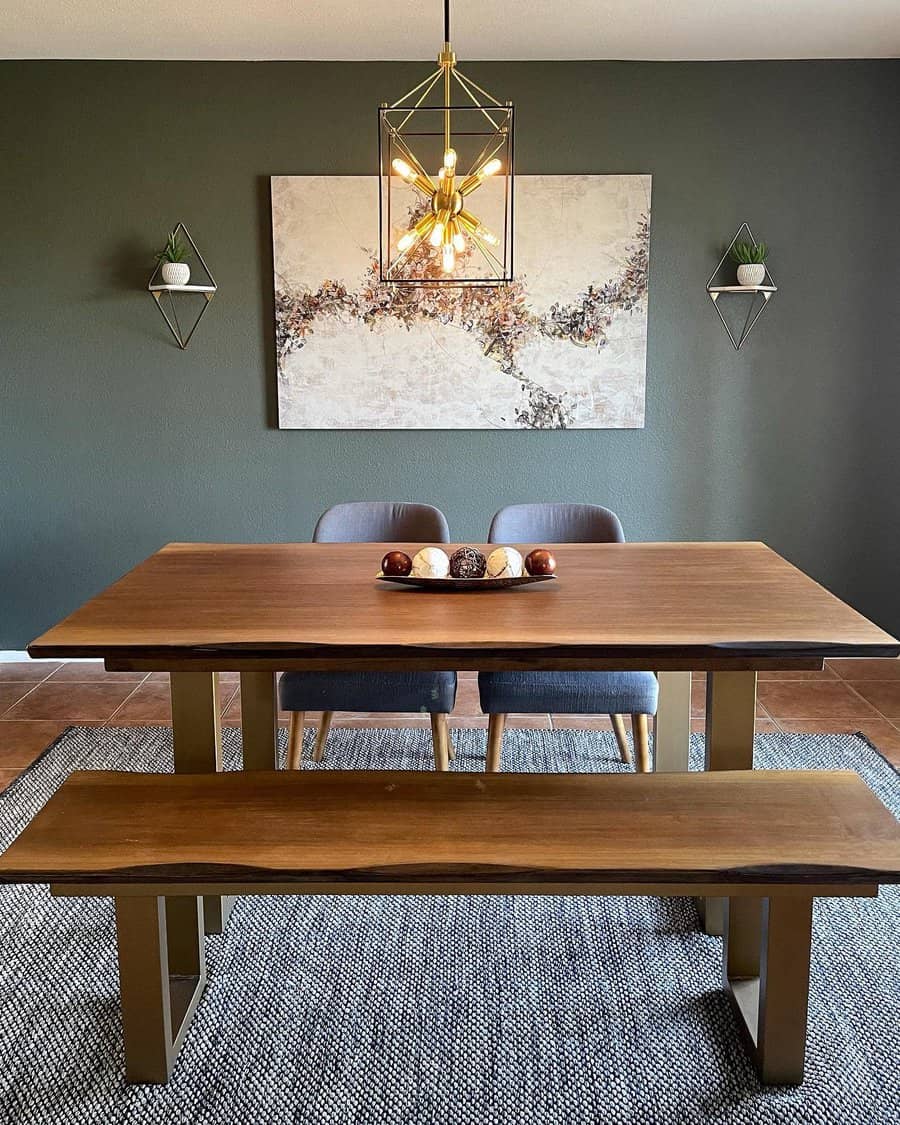 Dining room with a wooden table, bench, and two chairs; modern light fixture, abstract art, and shelves with plants on the dark wall