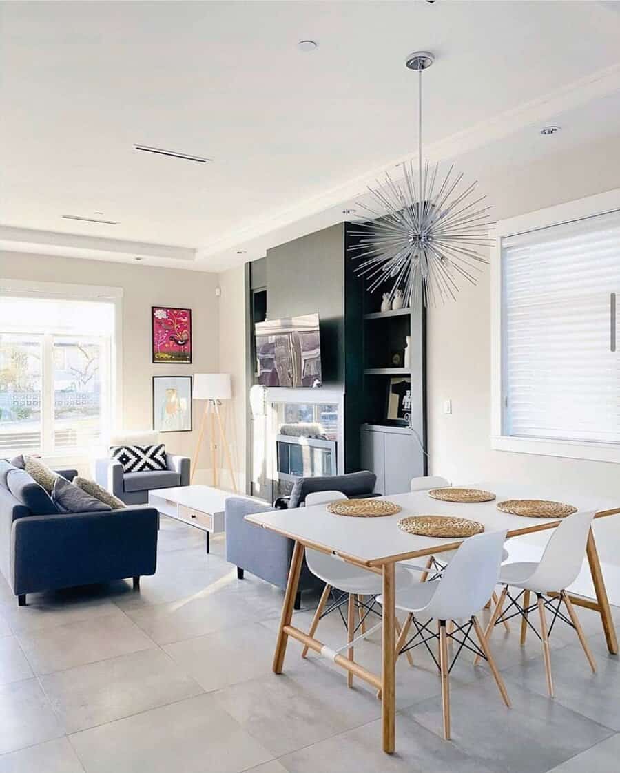 Modern living room with a gray sofa, dining table with white chairs, spiky chandelier, and a black accent wall with shelves and TV