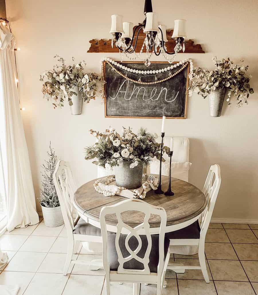 Cozy dining area with a round table, floral arrangements, a chandelier, and a chalkboard with "Amen" written on it in rustic decor style