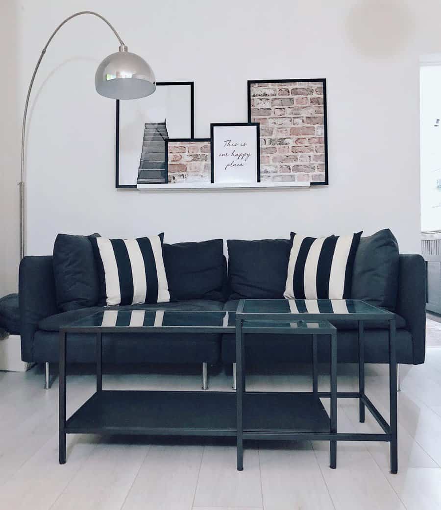 Modern living room with a dark sofa, striped pillows, a glass coffee table, a floor lamp, and framed wall art