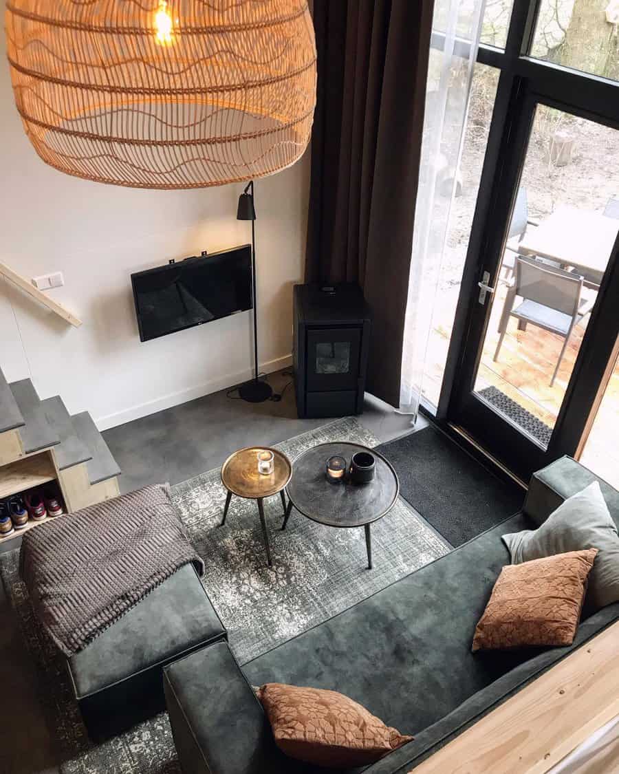 Modern tiny living room with a dark green sectional, warm-toned pillows, woven pendant lighting, and large glass doors for an open, airy feel