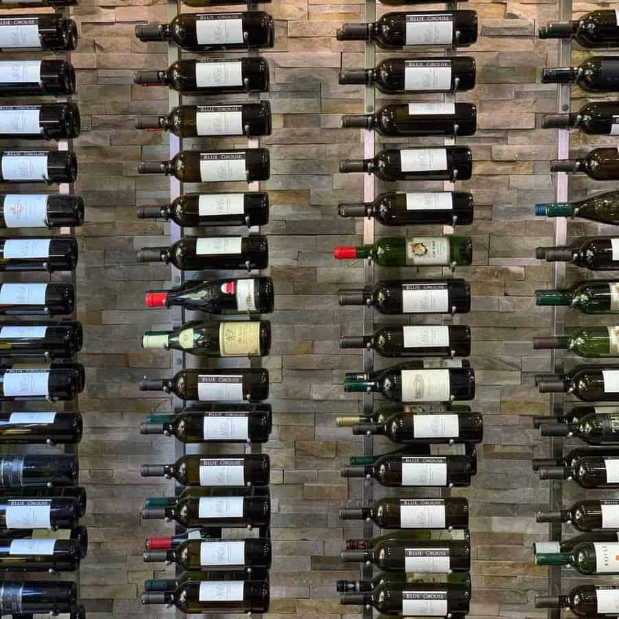 Rows of wine bottles displayed horizontally on a textured stone wall, featuring various labels and colors