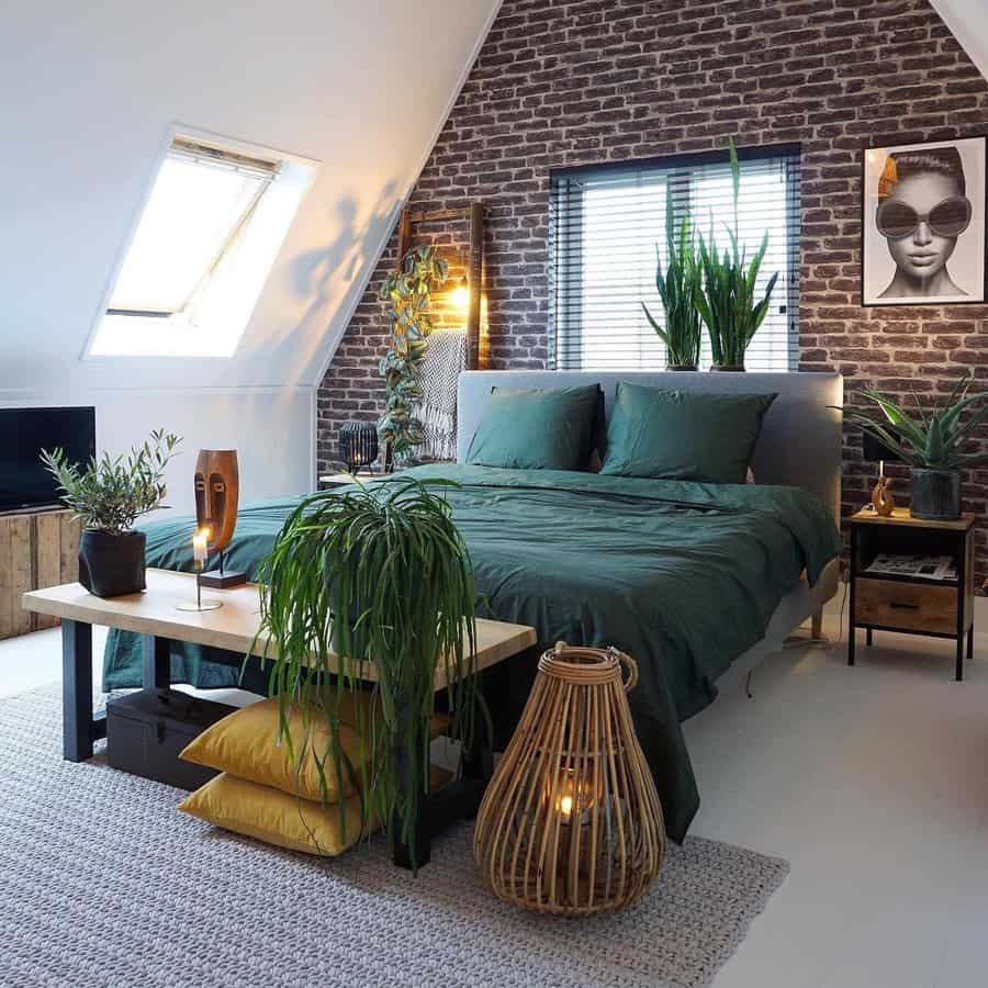 Modern Zen bedroom with an exposed brick wall, deep green bedding, lush plants, and warm lighting for a cozy yet industrial-chic retreat