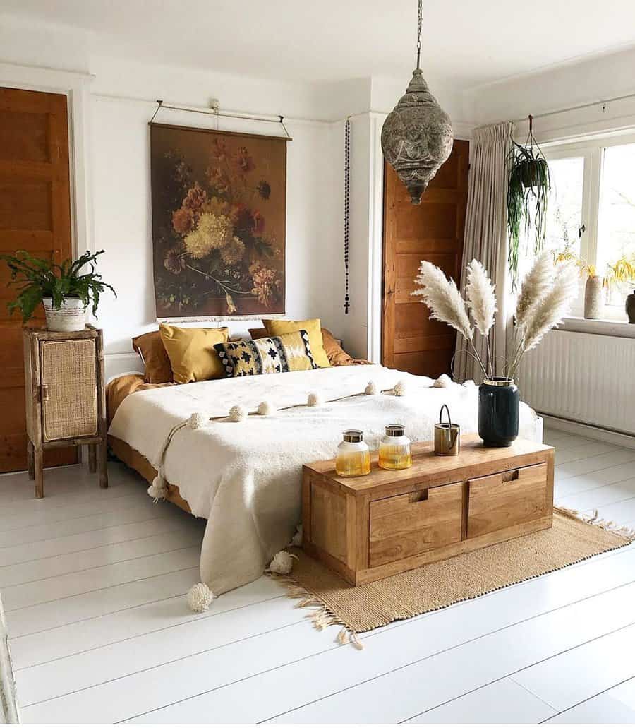 Cozy bedroom with a boho style, featuring a bed with yellow pillows, pampas grass, and a wooden bench on a white floor