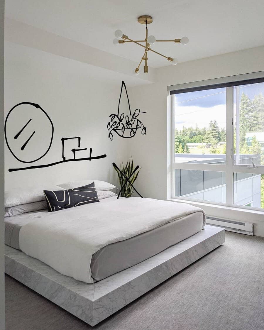 Minimalist bedroom with a large bed, geometric chandelier, and large window featuring wall art that includes a round mirror and potted plant drawings