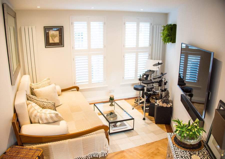 Stylish wooden daybed with neutral cushions, a glass coffee table, and a cozy living space featuring a drum set and modern decor