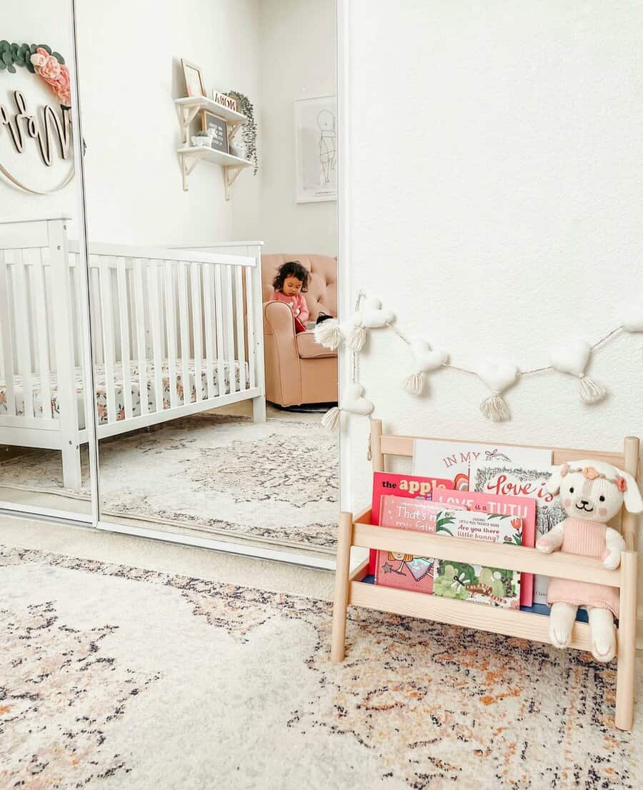 Soft and cozy nursery with a small wooden book rack filled with children's books and a plush bunny, next to a white crib and pastel decor.