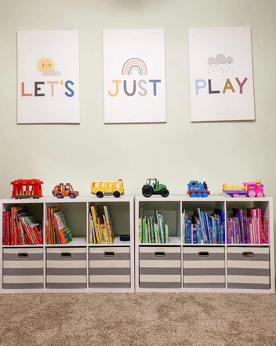 Colorful children's books neatly arranged in white cube shelves with striped storage bins, topped with toy vehicles, under "Let's Just Play" wall art.