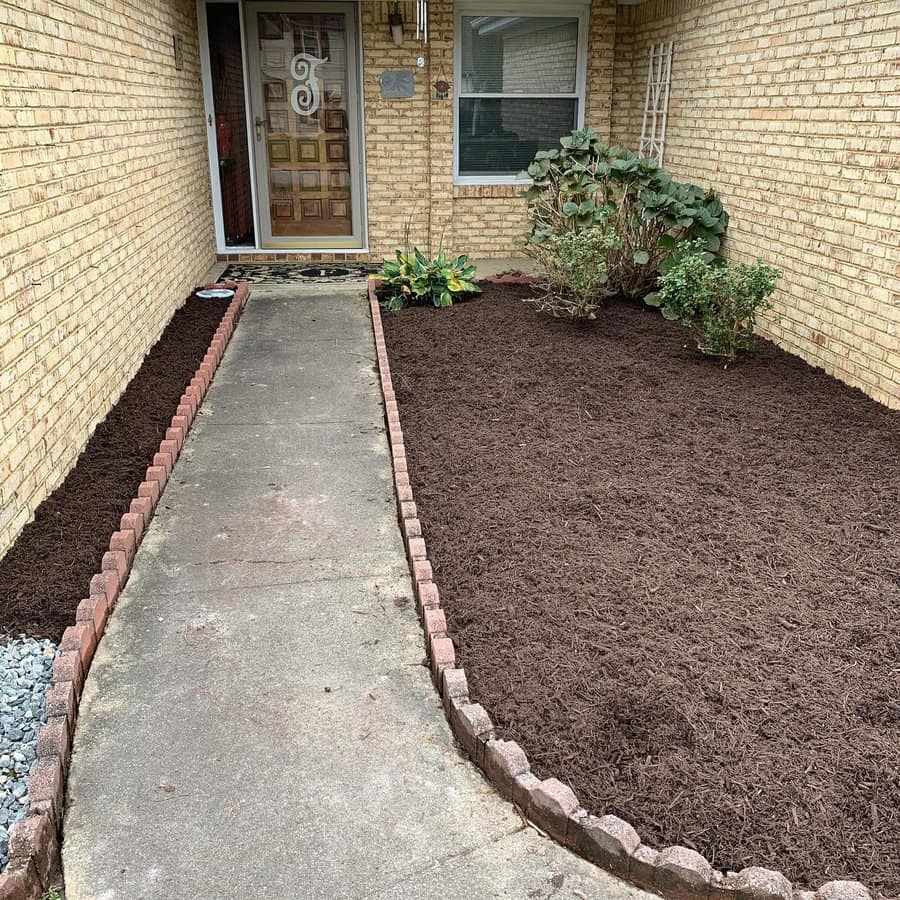 Simple front yard entryway with fresh mulch, brick edging along the path, and minimal plants creating a clean and tidy look