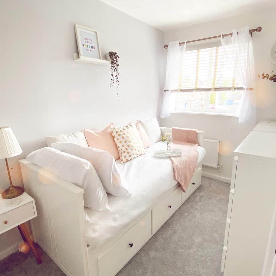 Bright and cozy white daybed with built-in storage, soft pastel pillows, and sheer curtains, creating a serene and inviting multipurpose space