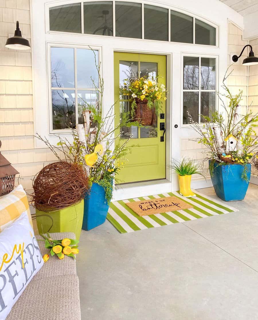 Front porch with a green door, colorful planters, a striped welcome mat, and spring-themed decorations including yellow flowers and pillows