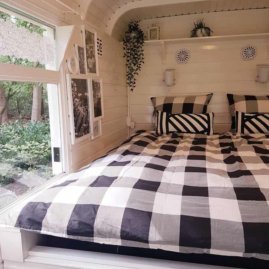 Cozy white room with a large window, black and white checkered bedding, and plants on a shelf above the bed