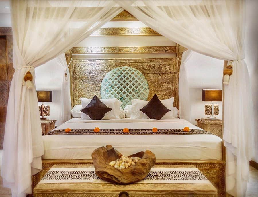 Luxurious bedroom with a canopy bed, decorative pillows, and elegant lamps, a wooden bowl centerpiece and ornate headboard add charm