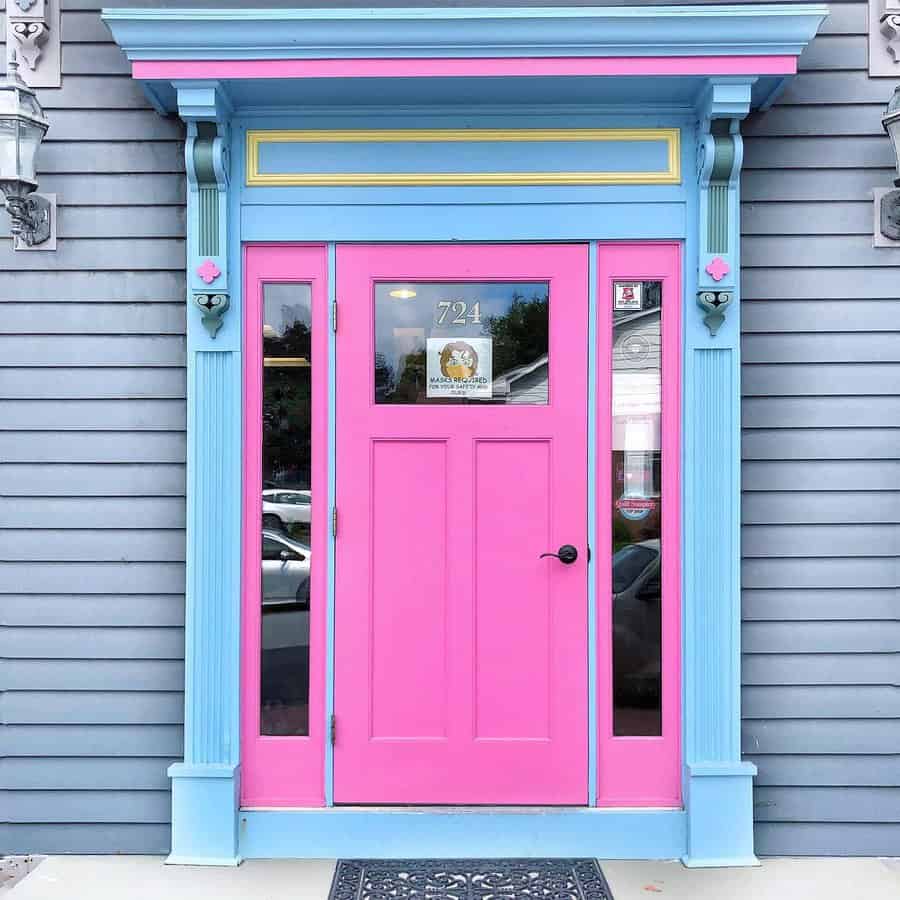 Bright pink door with blue trim on a gray building facade, featuring small decorative details and a glass panel