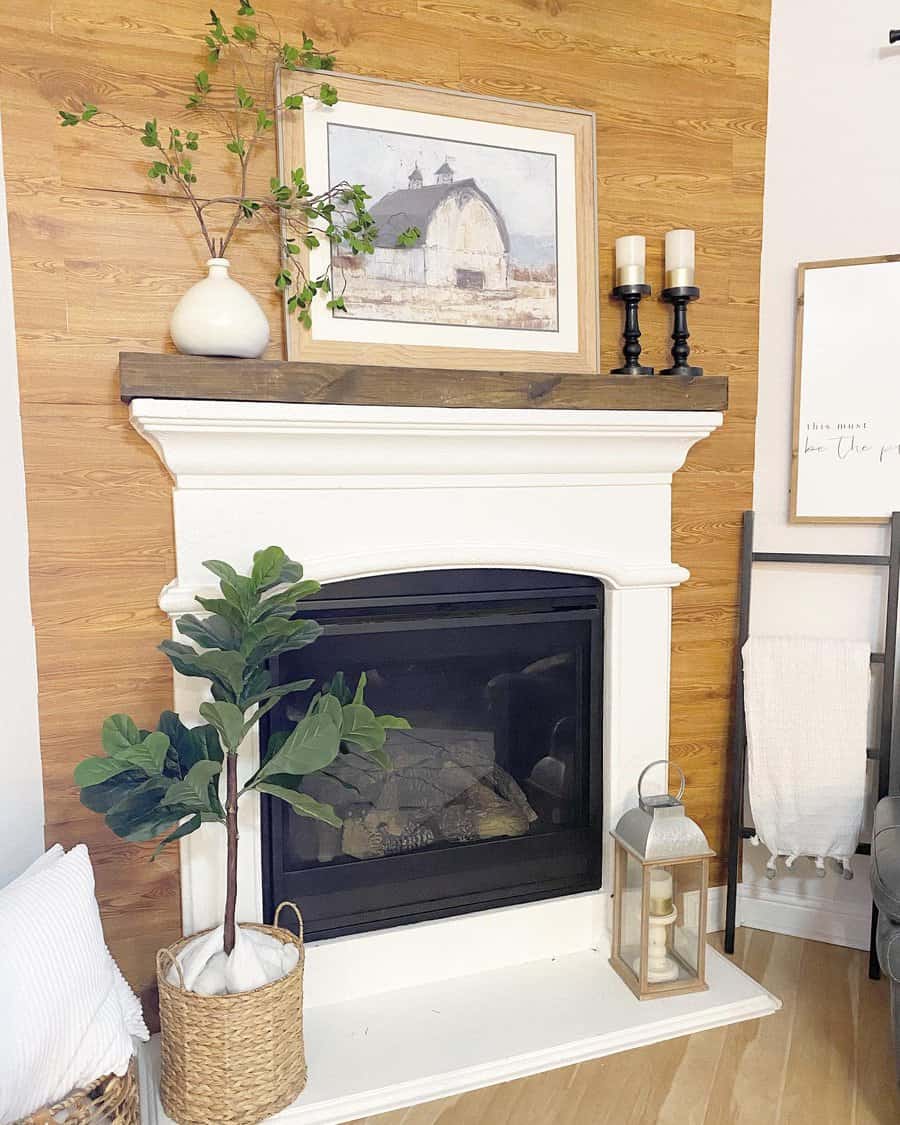 Cozy living room with a white fireplace, wooden mantel, rustic decor, and a potted plant. Art and candles adorn the mantel