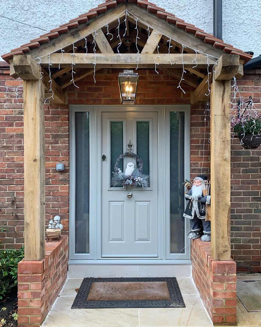 Front door with a small porch, festive decorations, wreath, and Santa figure; brick walls and hanging lights create a cozy holiday feel