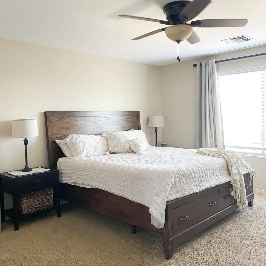 Bedroom with a wooden bed, light bedding, two side tables with lamps, a ceiling fan, and a window with curtains