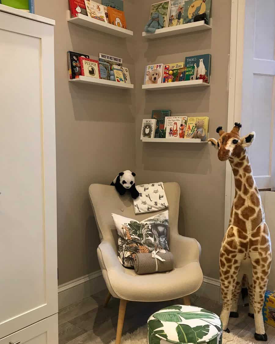 Cozy nursery reading nook with floating bookshelves, a beige accent chair with jungle-themed pillows, and a large plush giraffe.