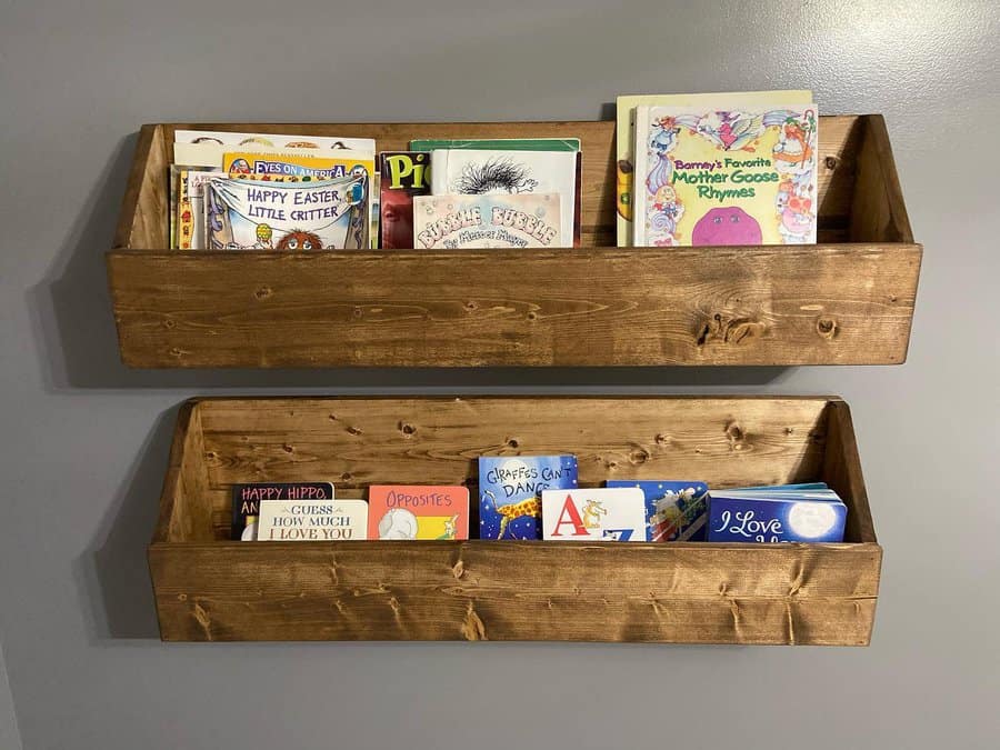 Wall-mounted wooden bookshelves holding colorful children's books, creating a rustic and organized reading space against a gray wall.