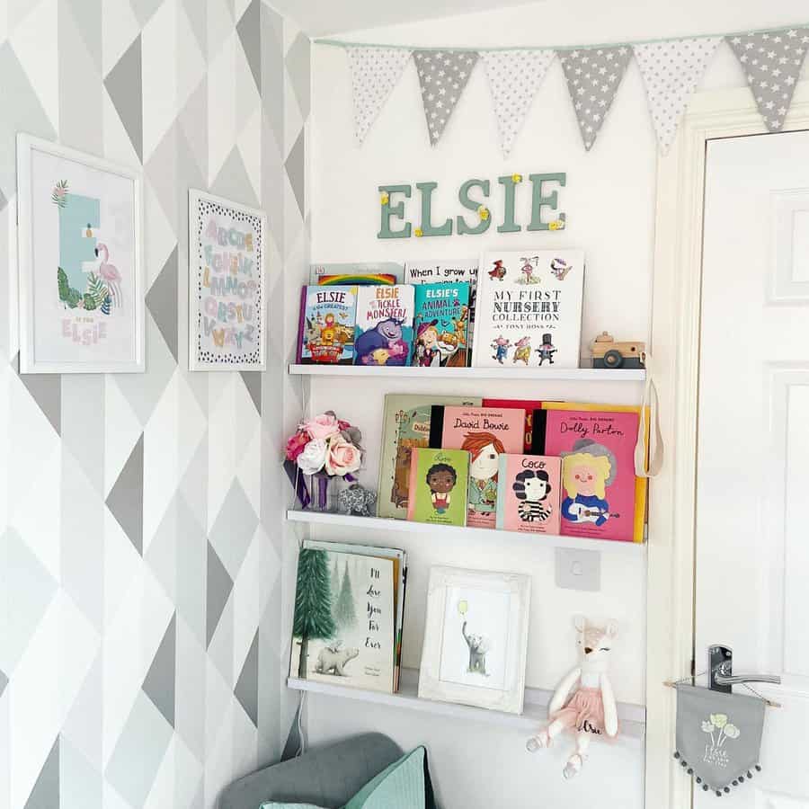 Charming nursery reading corner with floating bookshelves, personalized name decor, soft pastel bunting, and a cozy seating area.