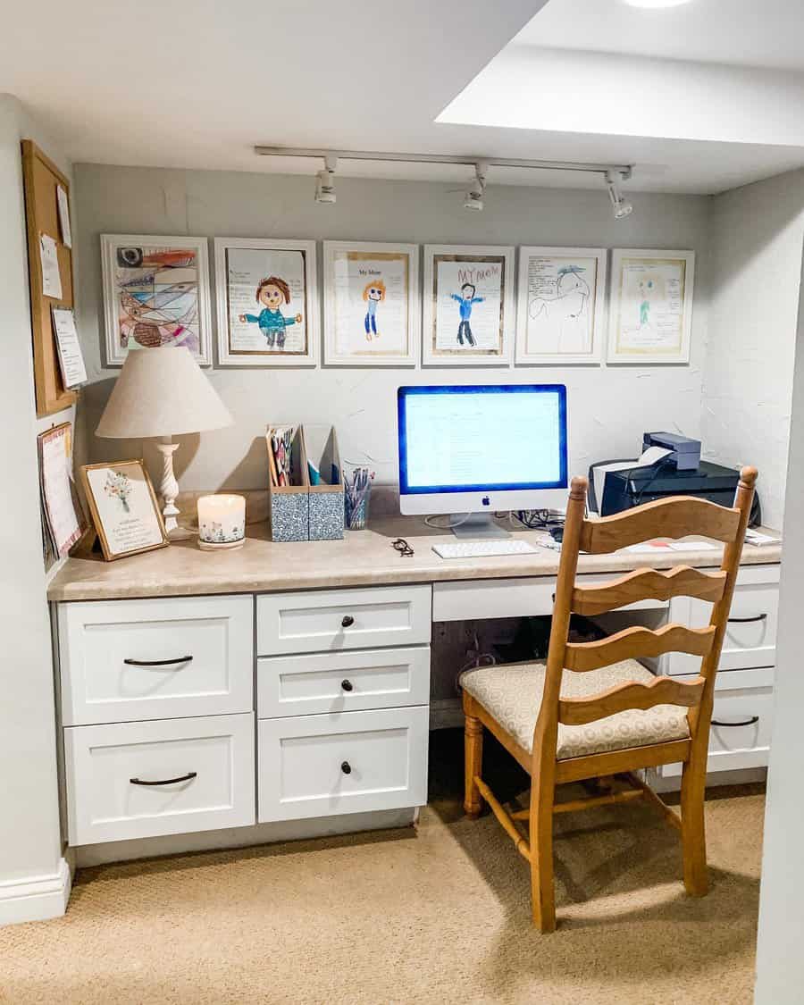 Cozy basement home office with built-in white cabinetry, warm lighting, personal artwork, and a compact yet functional workspace.