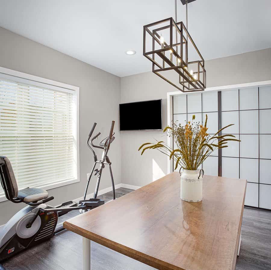 Bright and modern basement office with a multipurpose space, featuring an exercise area, a sleek wooden table, and stylish lighting for a functional design.