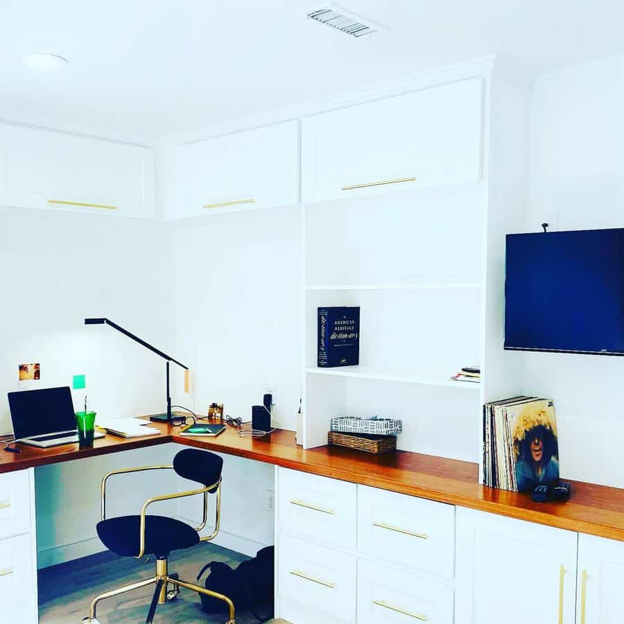 Elegant basement office with built-in white cabinetry, warm wood countertops, gold accents, and a sleek workspace for a modern and organized setup.