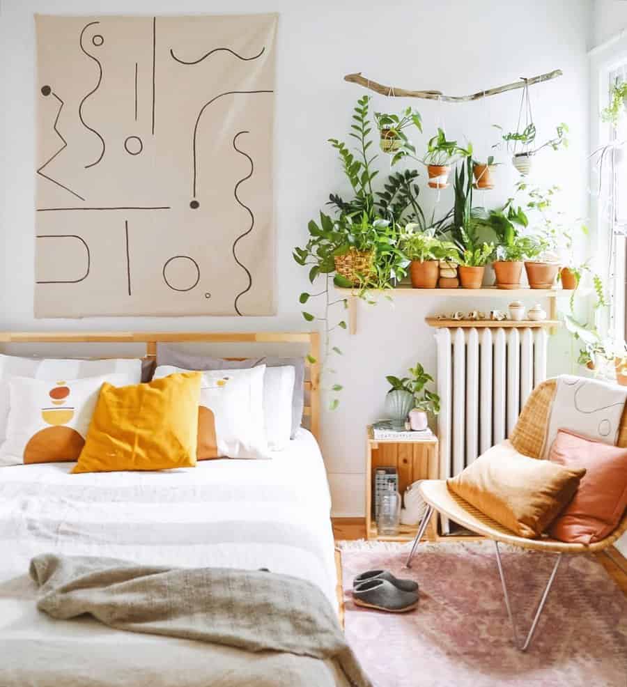 Bright bedroom with a modern abstract wall tapestry, potted plants on shelves, a cozy bed with colorful pillows, and a wooden chair