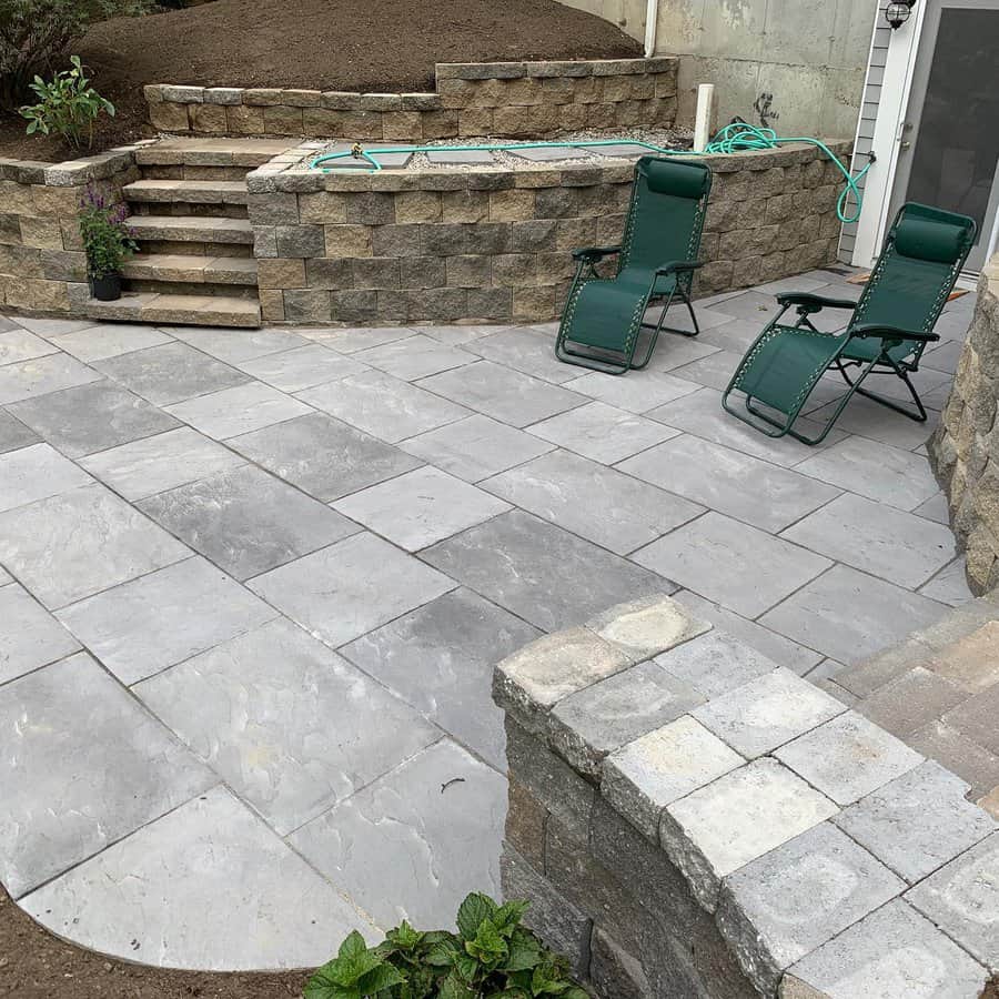 Modern backyard patio with large gray stone pavers, built-in retaining walls, and reclining chairs for a sleek and relaxing outdoor space