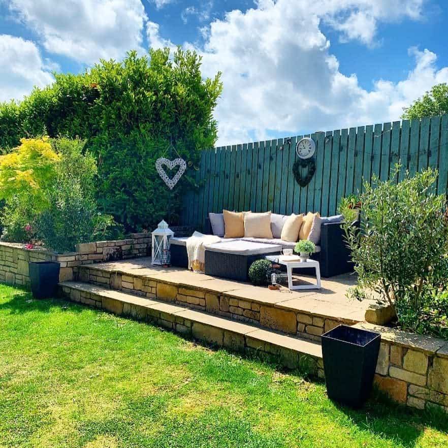 Charming backyard patio with stone pavers, a cozy outdoor sofa, lush greenery, and decorative accents for a relaxing garden retreat