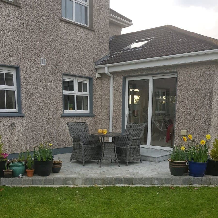 Cozy backyard patio with gray stone pavers, wicker seating, potted flowers, and a charming outdoor dining area for a relaxing garden retreat