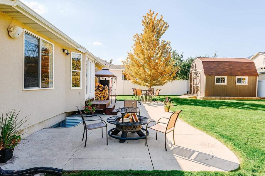 Spacious backyard with a smooth concrete patio, fire pit seating, a cozy dining area, and a charming shed, surrounded by lush greenery