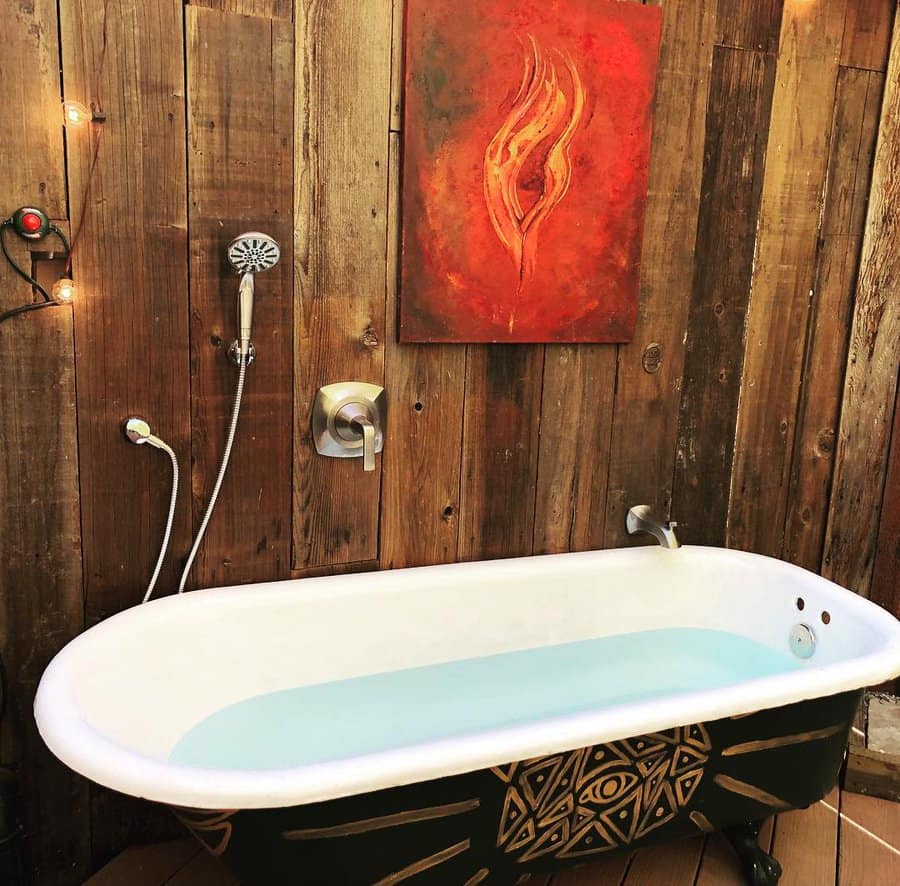 Rustic outdoor bathtub with tribal design, set against a wooden wall with warm lighting and bold red artwork