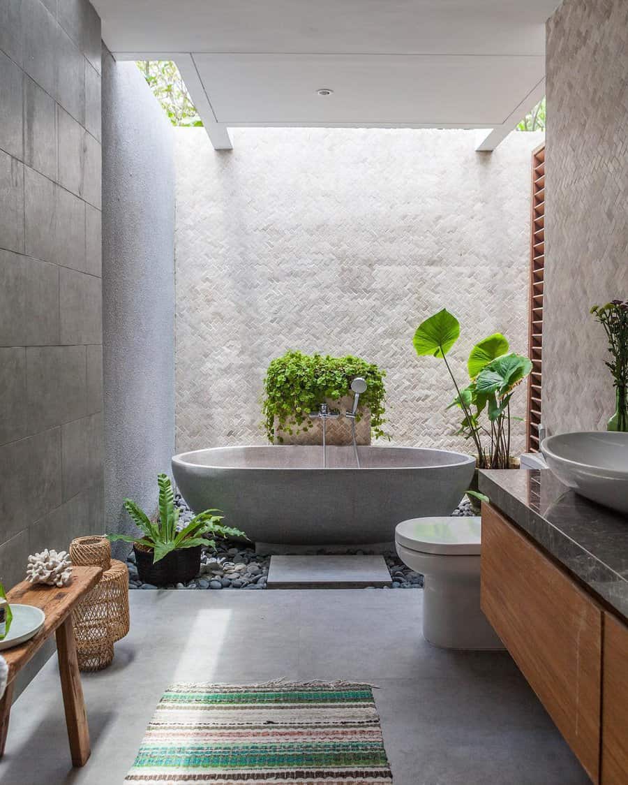 Modern outdoor bathroom with a freestanding tub, greenery, and natural light from an open ceiling, featuring minimalist decor with wood accents