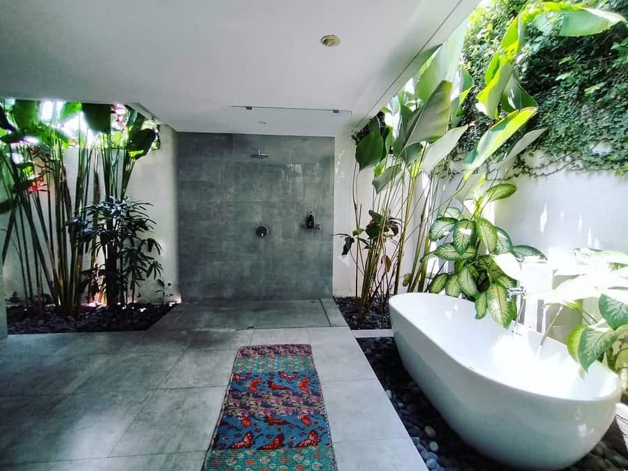 Modern outdoor bathroom with a freestanding tub, rain shower, and lush greenery, creating a serene spa-like retreat