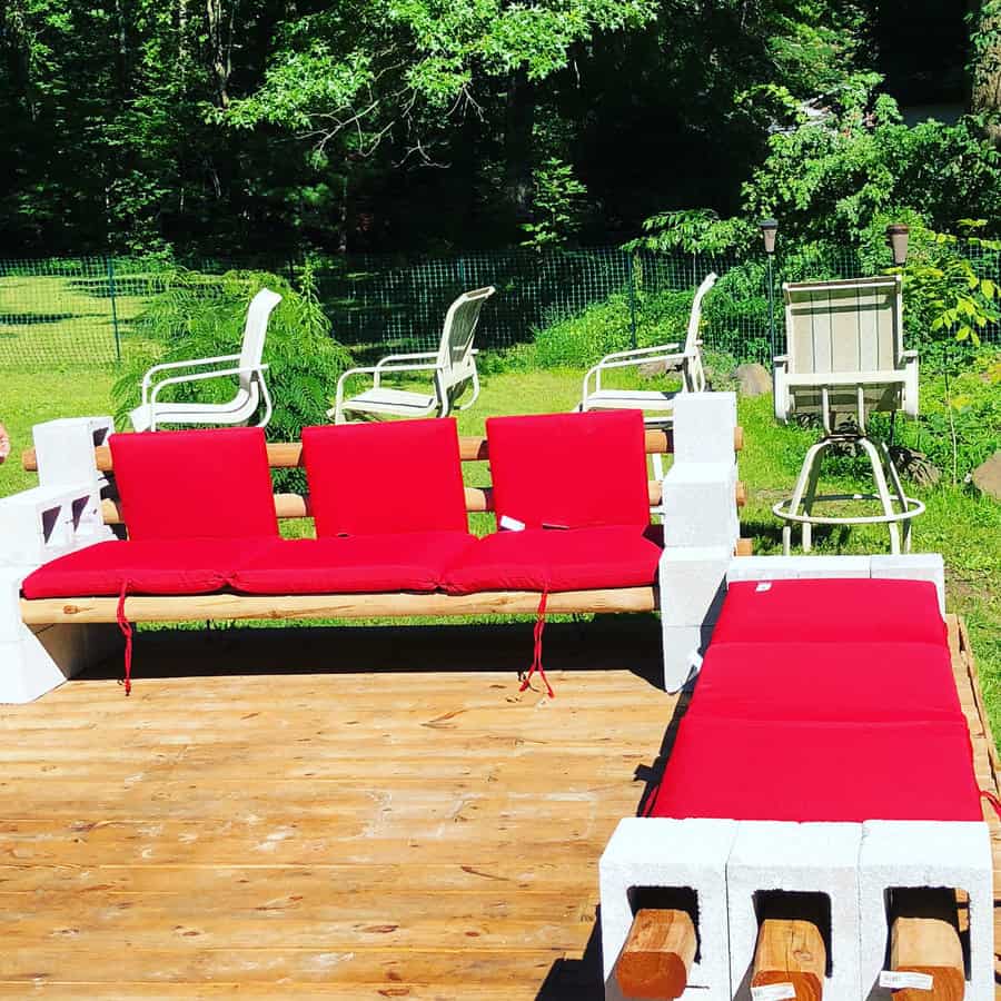 DIY outdoor cinder block bench and lounger with wooden beams and bold red cushions, creating a stylish and comfortable seating area on a wooden deck