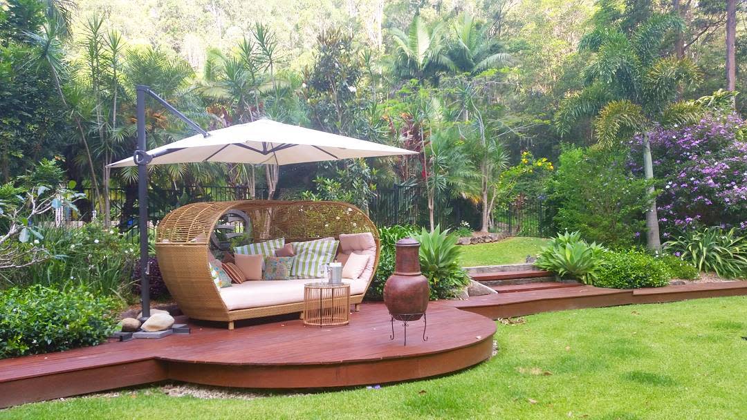 Tropical outdoor daybed with a woven rattan frame, plush cushions, and a large umbrella, creating a relaxing retreat on a wooden deck