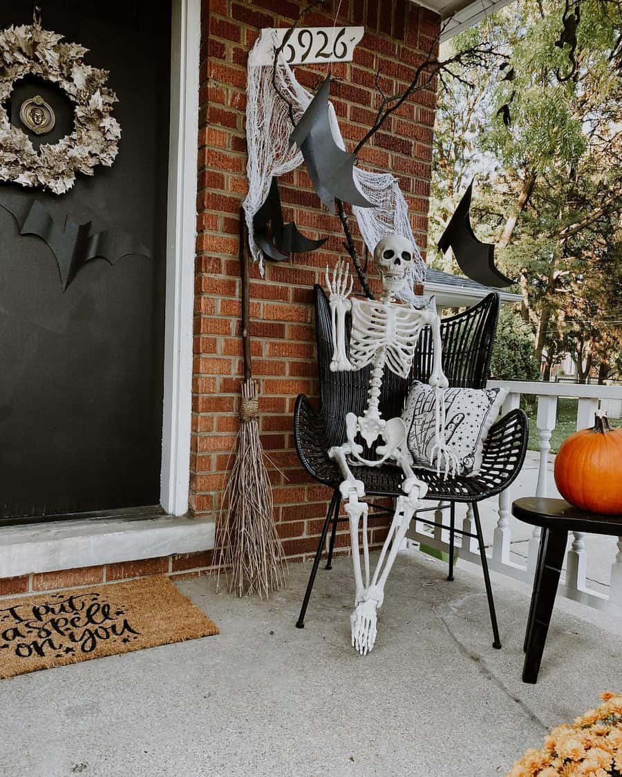 A porch decorated for Halloween with a skeleton, bats, broomstick, and pumpkin