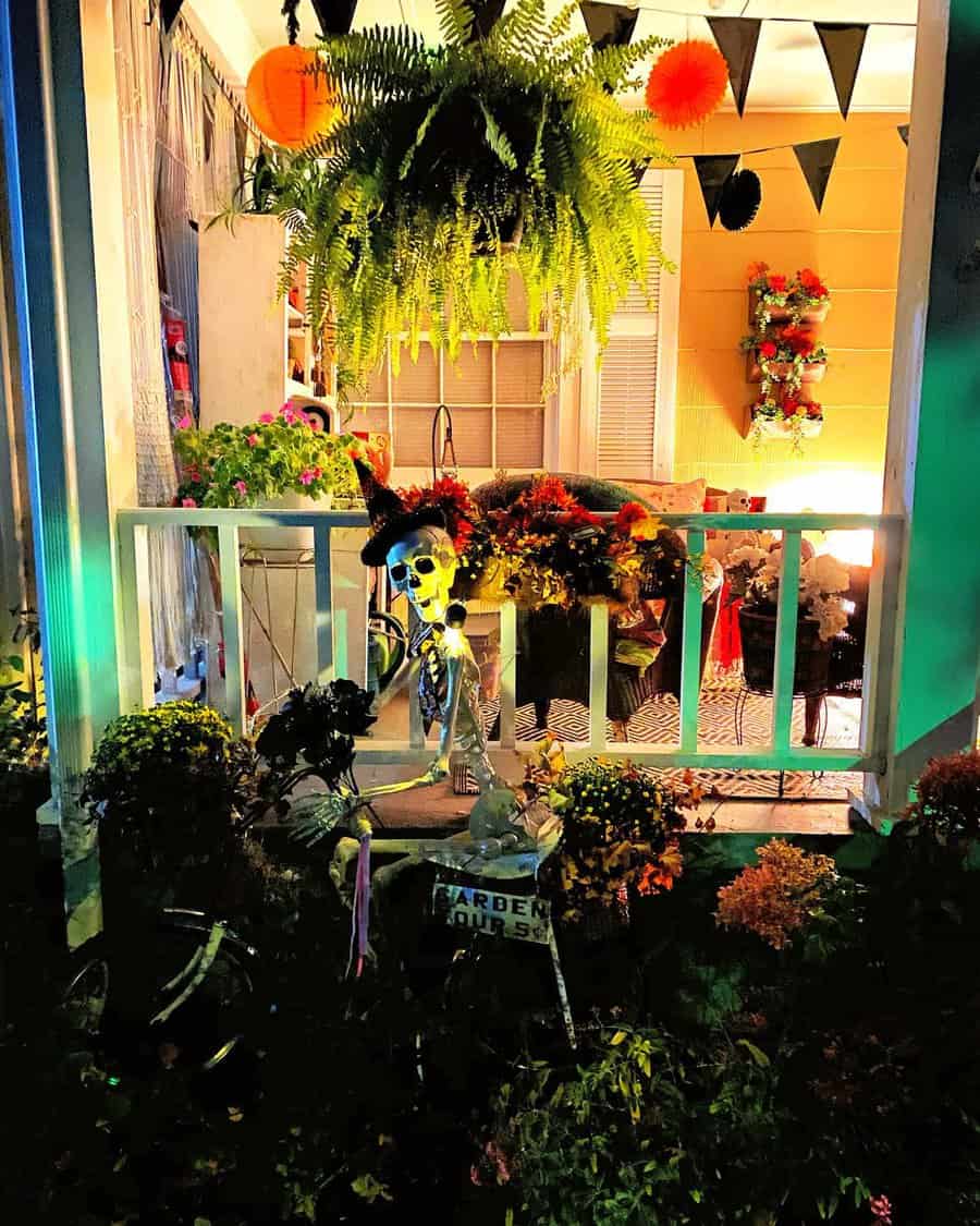 A porch decorated for Halloween with a skeleton wearing a hat and lots of plants