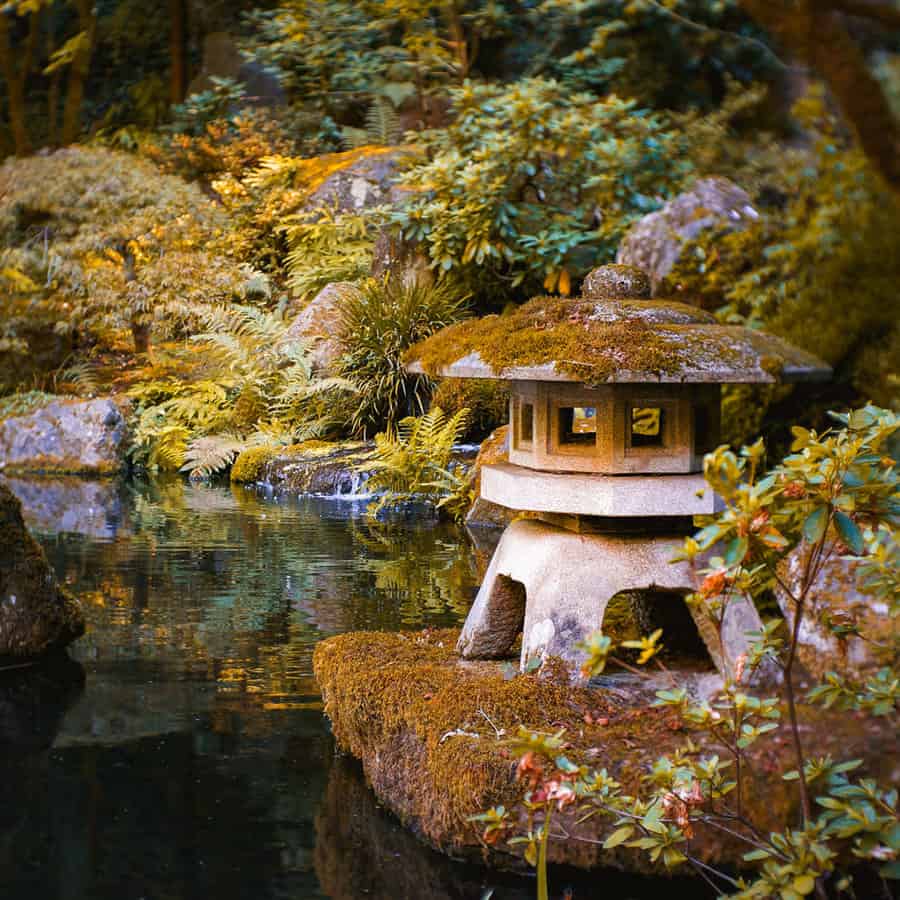 Stone lantern by a serene pond in a lush Japanese garden with moss-covered rocks and greenery