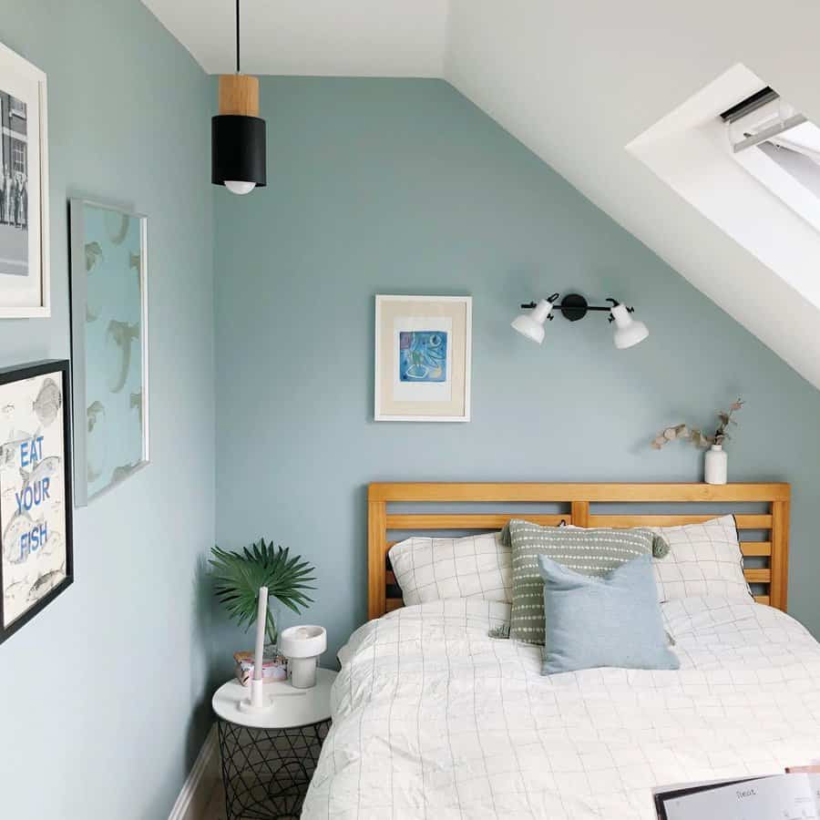 Fresh attic bedroom with soft blue walls, natural wood furniture, and cozy textiles. Skylight and modern lighting add brightness to the space.