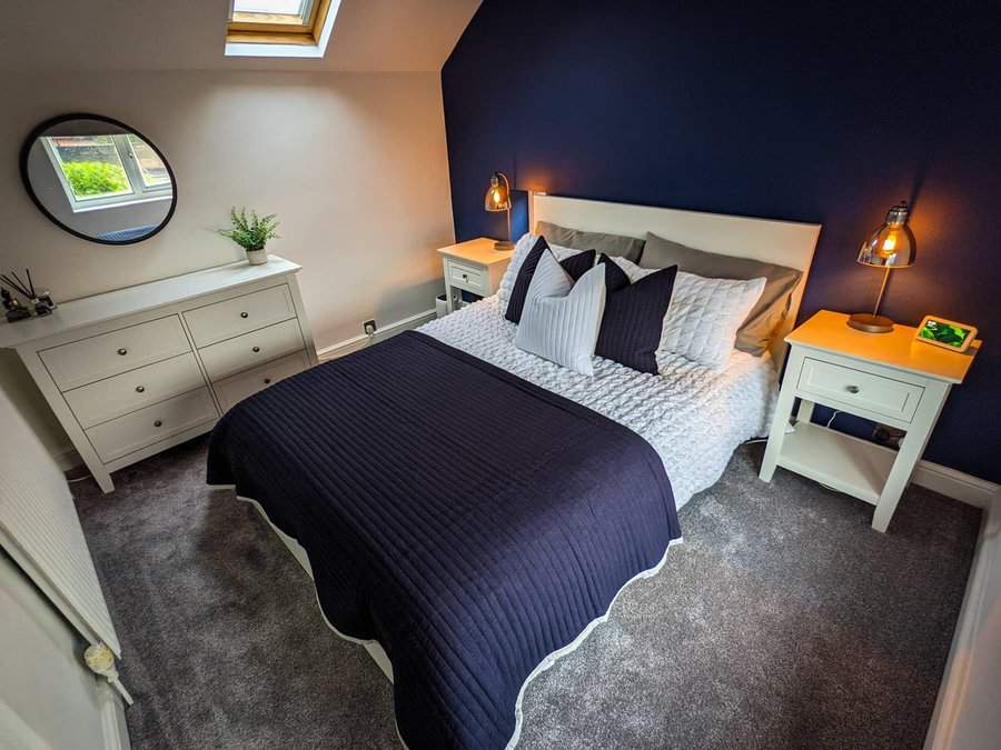 Elegant attic bedroom with a deep navy accent wall, soft lighting, and cozy textures. White furniture and warm tones create a balanced, inviting space.