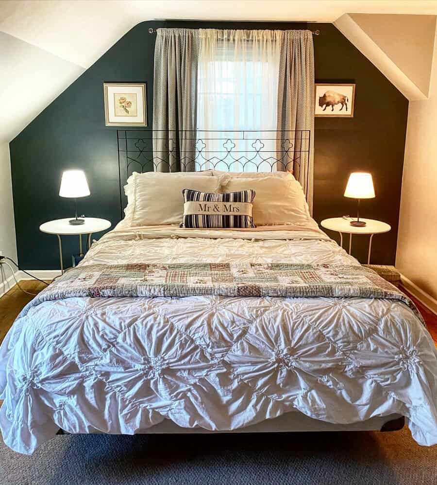 Cozy attic bedroom with a deep green accent wall, vintage iron bed frame, and soft layered bedding. Warm lighting and rustic decor create a charming retreat.