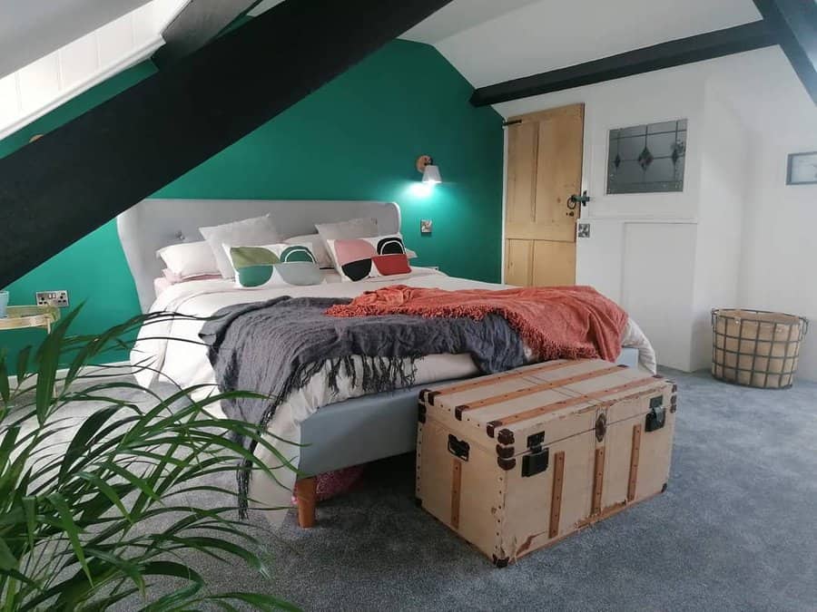 Vibrant attic bedroom with a bold teal accent wall, exposed beams, and a vintage trunk. Cozy textiles and eclectic decor create a stylish retreat.