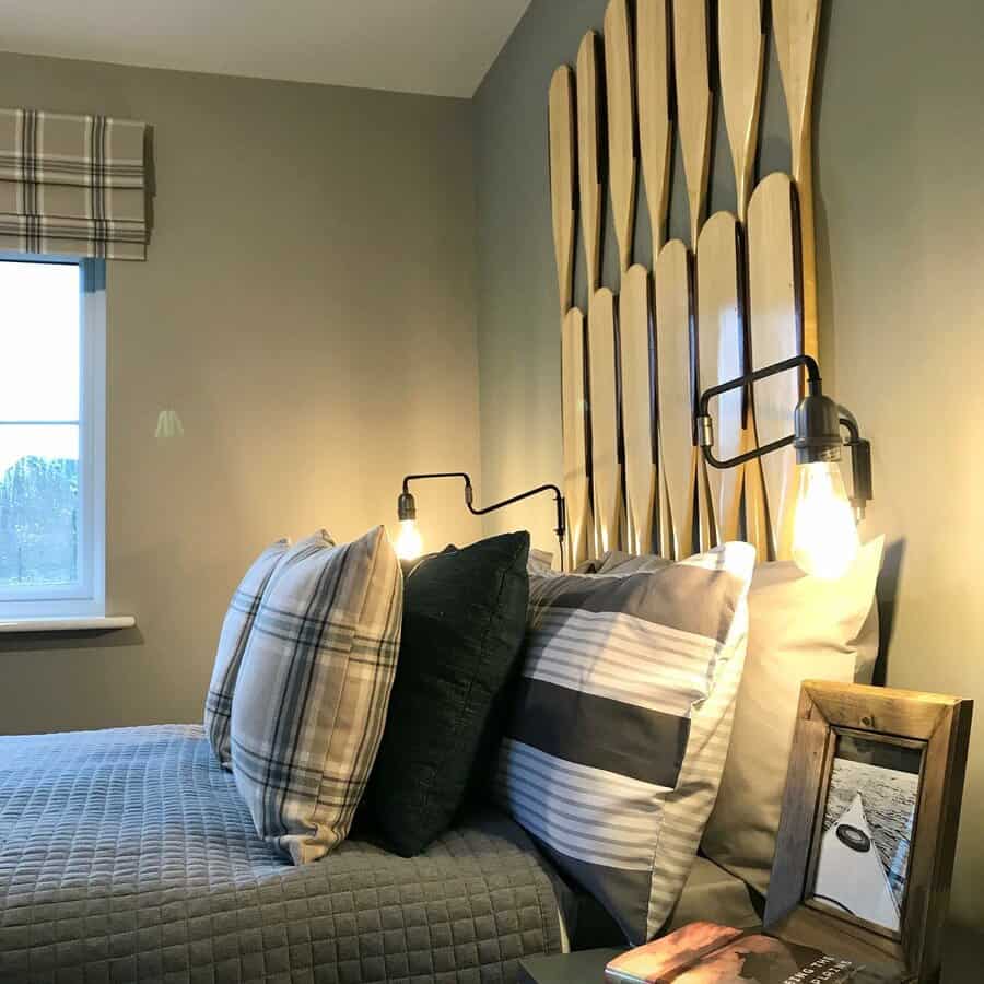 Bedroom with a paddle-themed headboard, plaid pillows, wall sconces, and a framed photo; natural light from a window on the left